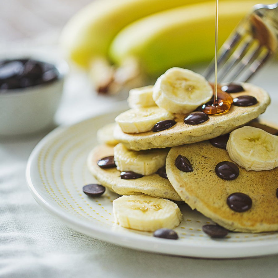 Gluten Free, Vegan Chocolate Chip Pancakes Topped with Sliced Bananas and Maple Syrup